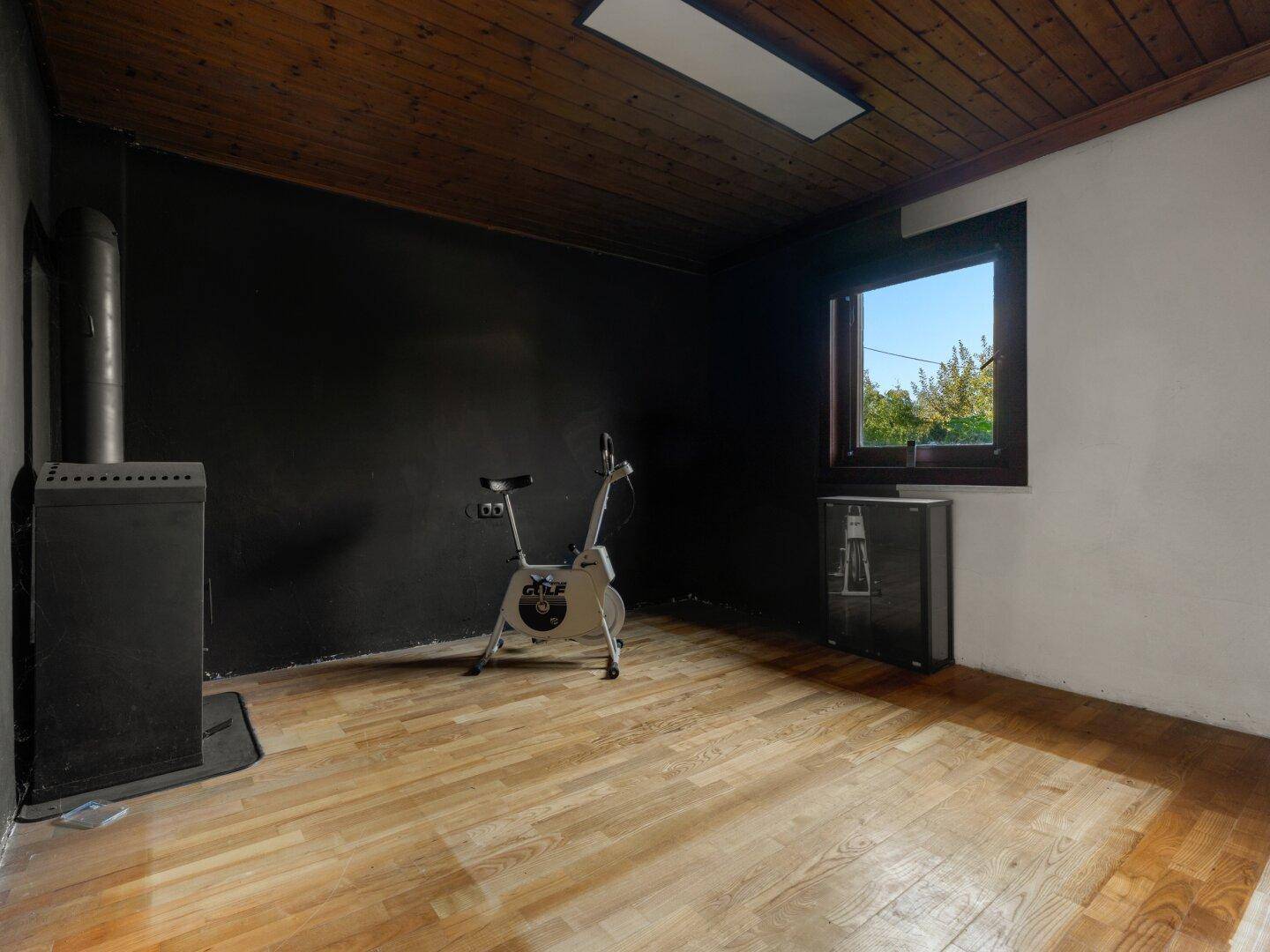 Raum mit Holzboden, Kaminofen und einem Heimtrainer, ideal als Hobby- oder Fitnessraum.