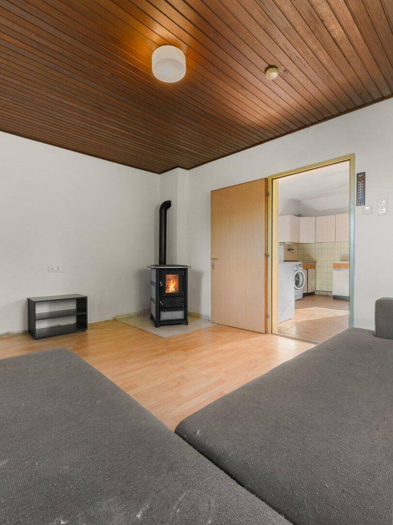 Wohnzimmer mit Holzbalkendecke, Laminatboden und einem modernen Kaminofen als Wärmequelle.