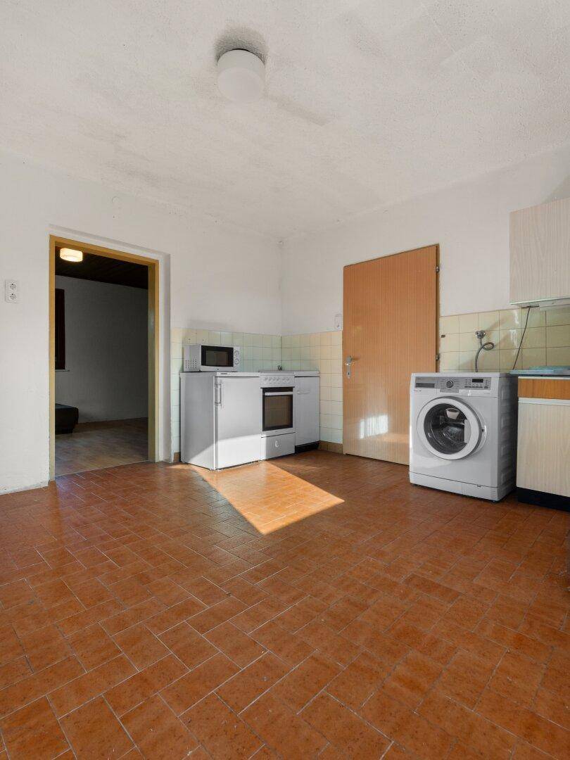 Einfache Küche mit Terrakotta-Fliesenboden, Waschmaschine und grundlegenden Küchengeräten.