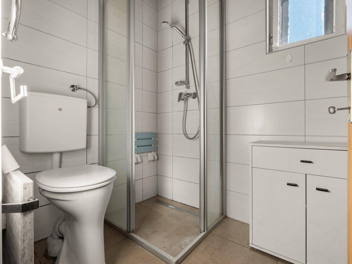 Funktionales Badezimmer mit Duschkabine, Toilette und Fenster für Tageslicht.