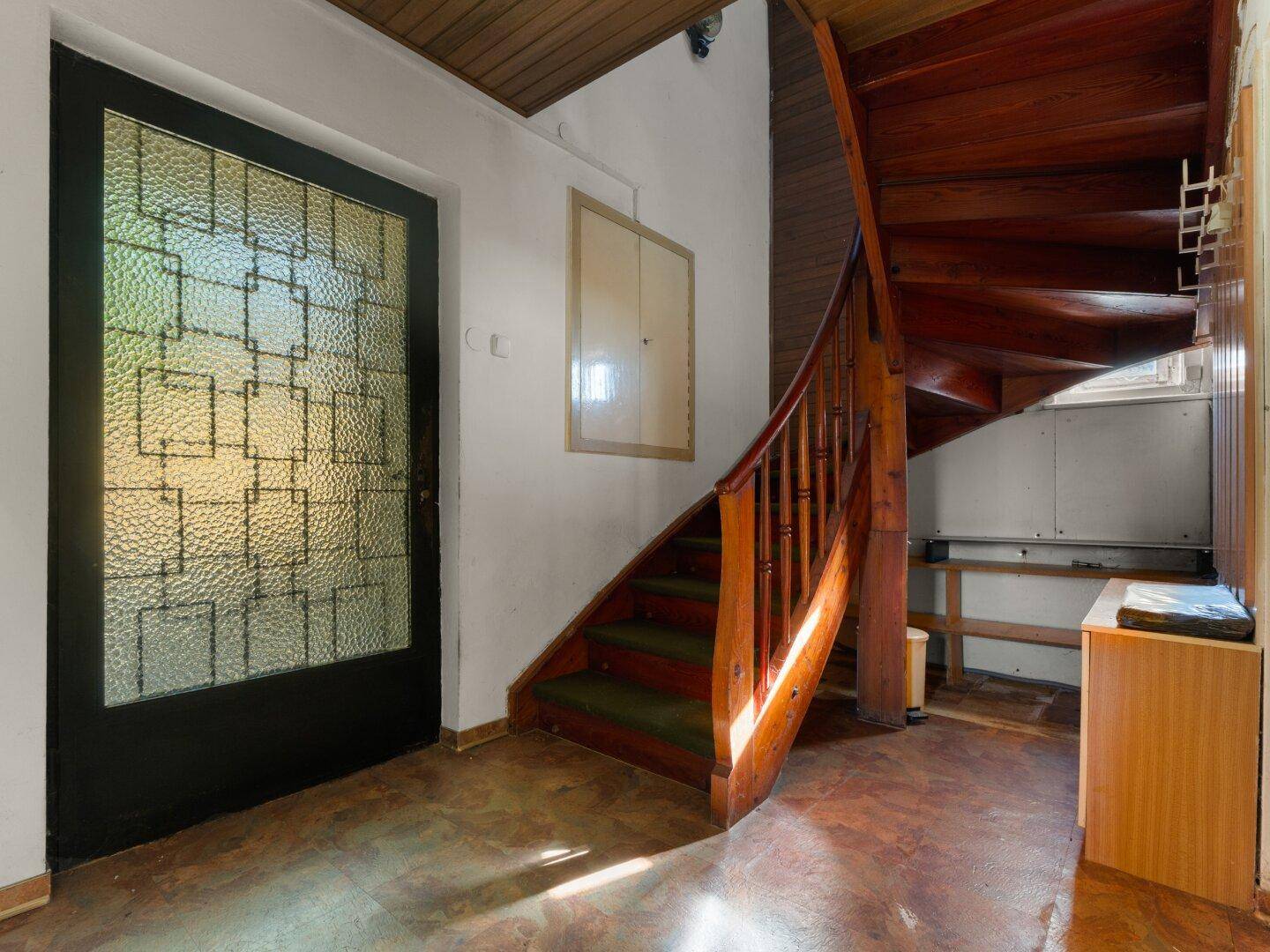 Heller Flur mit einer eleganten Holztreppe und einer verzierten Eingangstür.