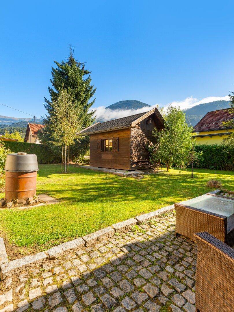 Idyllischer Gartenbereich mit Holzschuppen, Rasenfläche und einer gemütlichen Outdoor-Sitzgruppe.