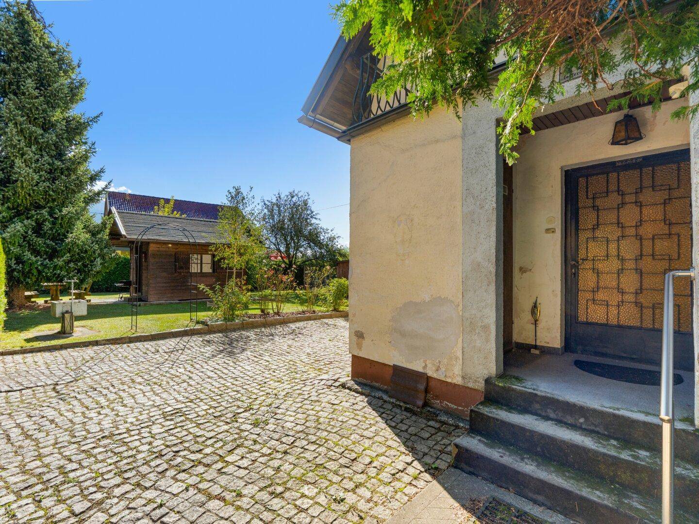 Eingangsbereich des Hauses mit Kopfsteinpflaster und Blick auf den Garten und Holzschuppen.