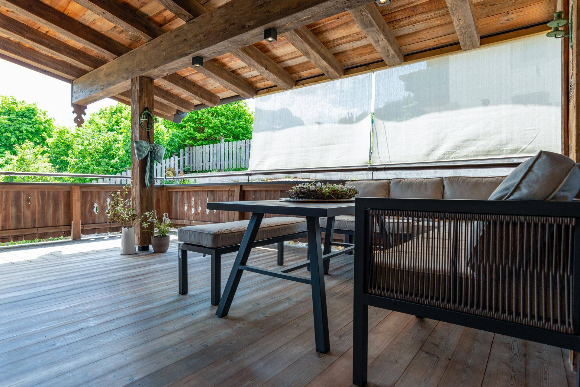 Überdachter Balkon mit Holzboden und bequemen Outdoor-Möbeln, ideal zum Entspannen.