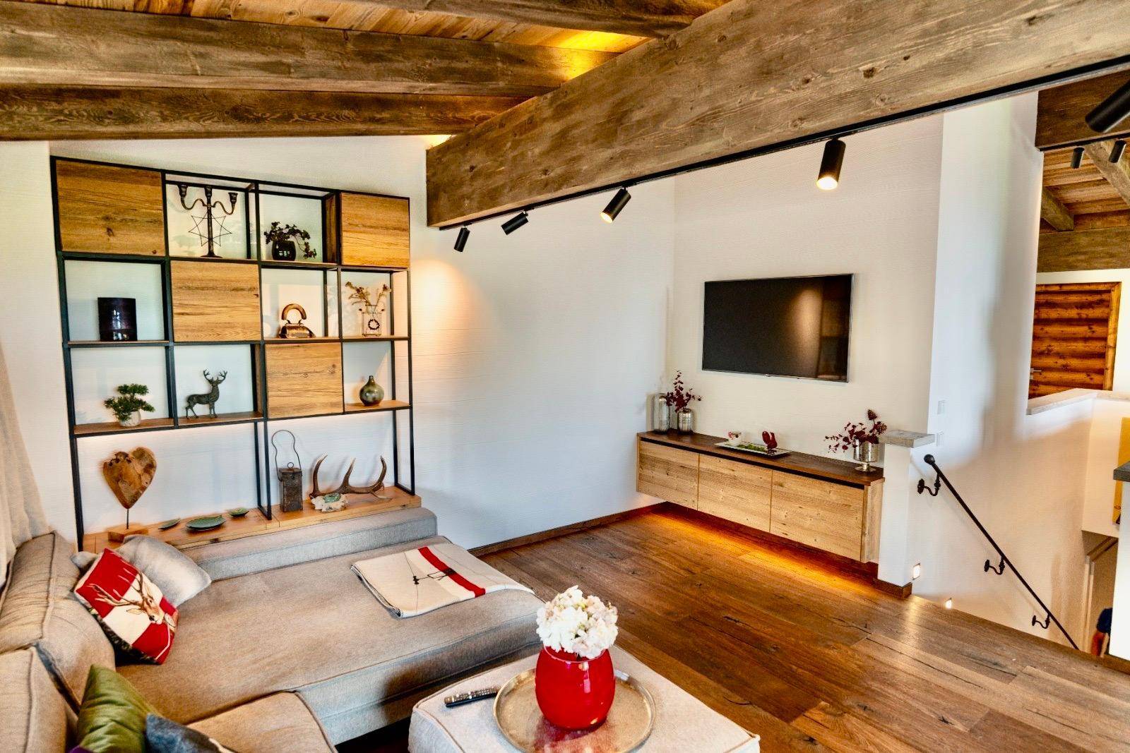 Gemütliches Wohnzimmer mit Holzbalkendecke, Sofa und Wandregal im alpinen Stil.