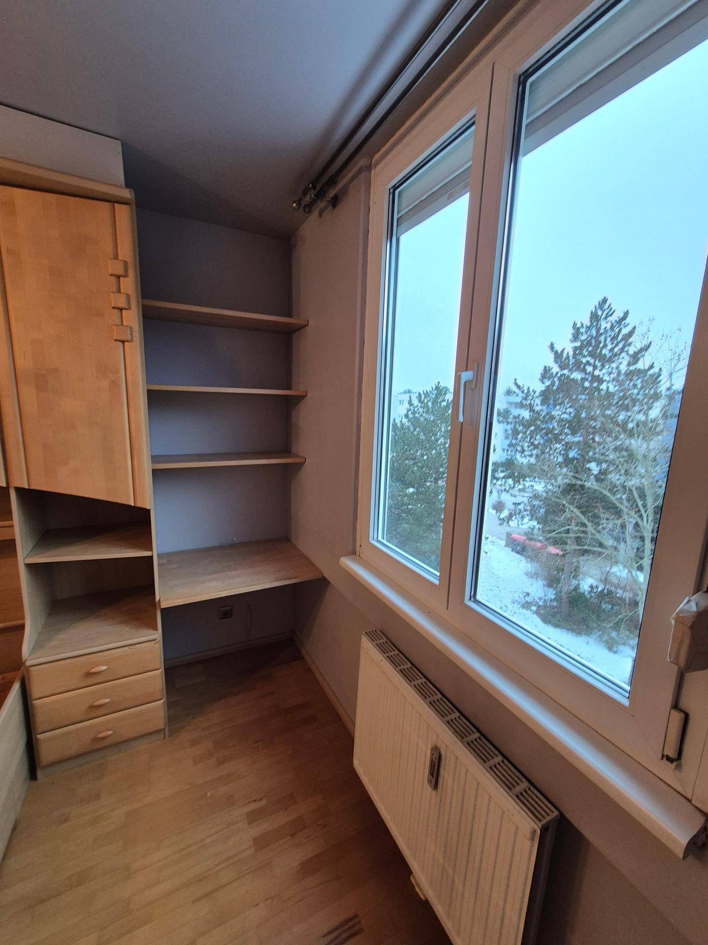 Schlafzimmer mit integrierten Regalen und großem Fenster, das viel Tageslicht hereinlässt.