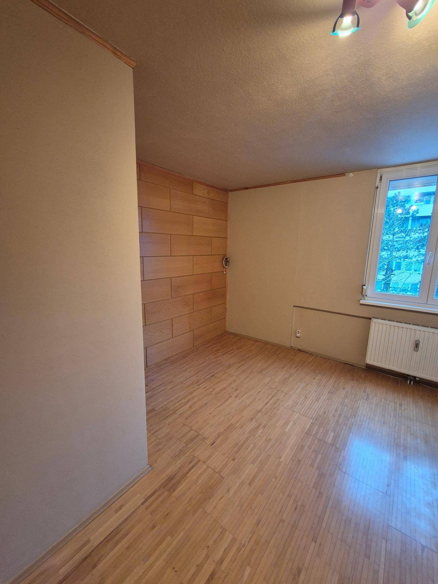 Geräumiges Wohnzimmer mit Holzwandverkleidung und großem Fenster für natürliche Belichtung.