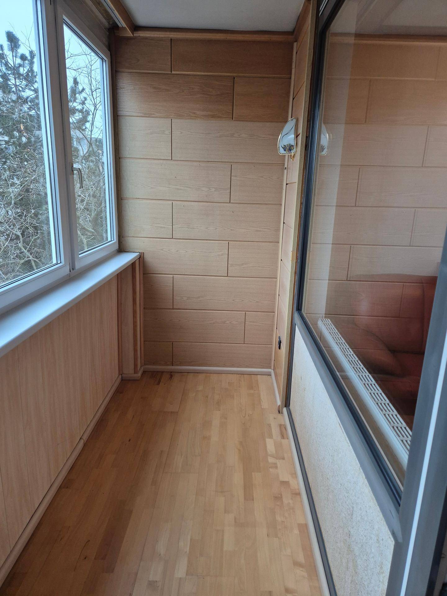 Verglaste Loggia mit Holzwandverkleidung und Parkettboden, ideal für entspannte Stunden.