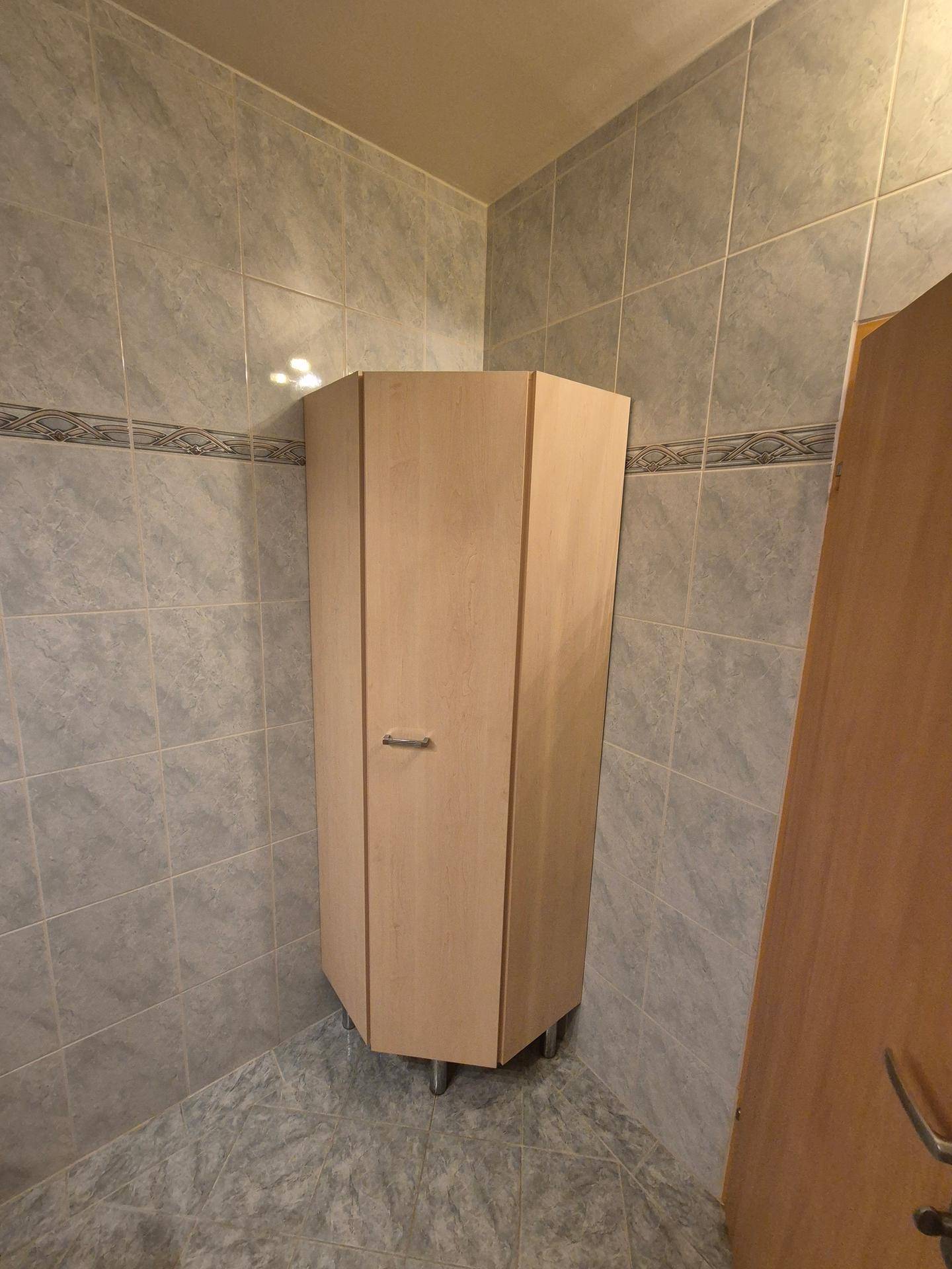 Eckschrank in einem gefliesten Badezimmer, der zusätzlichen Stauraum bietet.