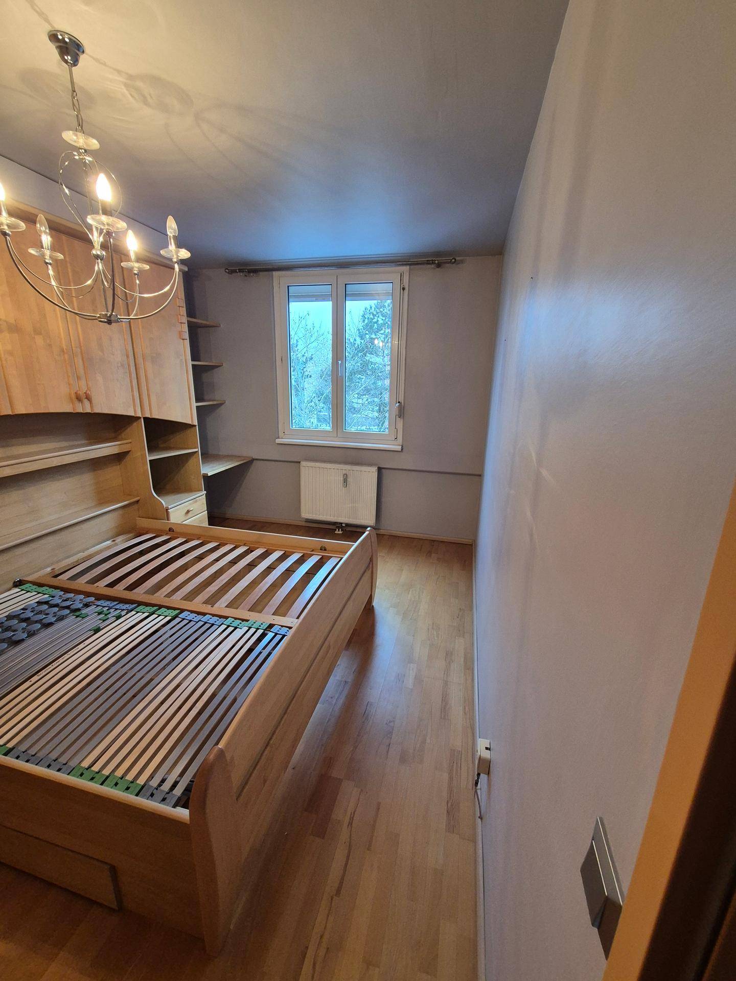 Helles Schlafzimmer mit Holzbettrahmen und Fenster, das den Blick nach draußen freigibt.