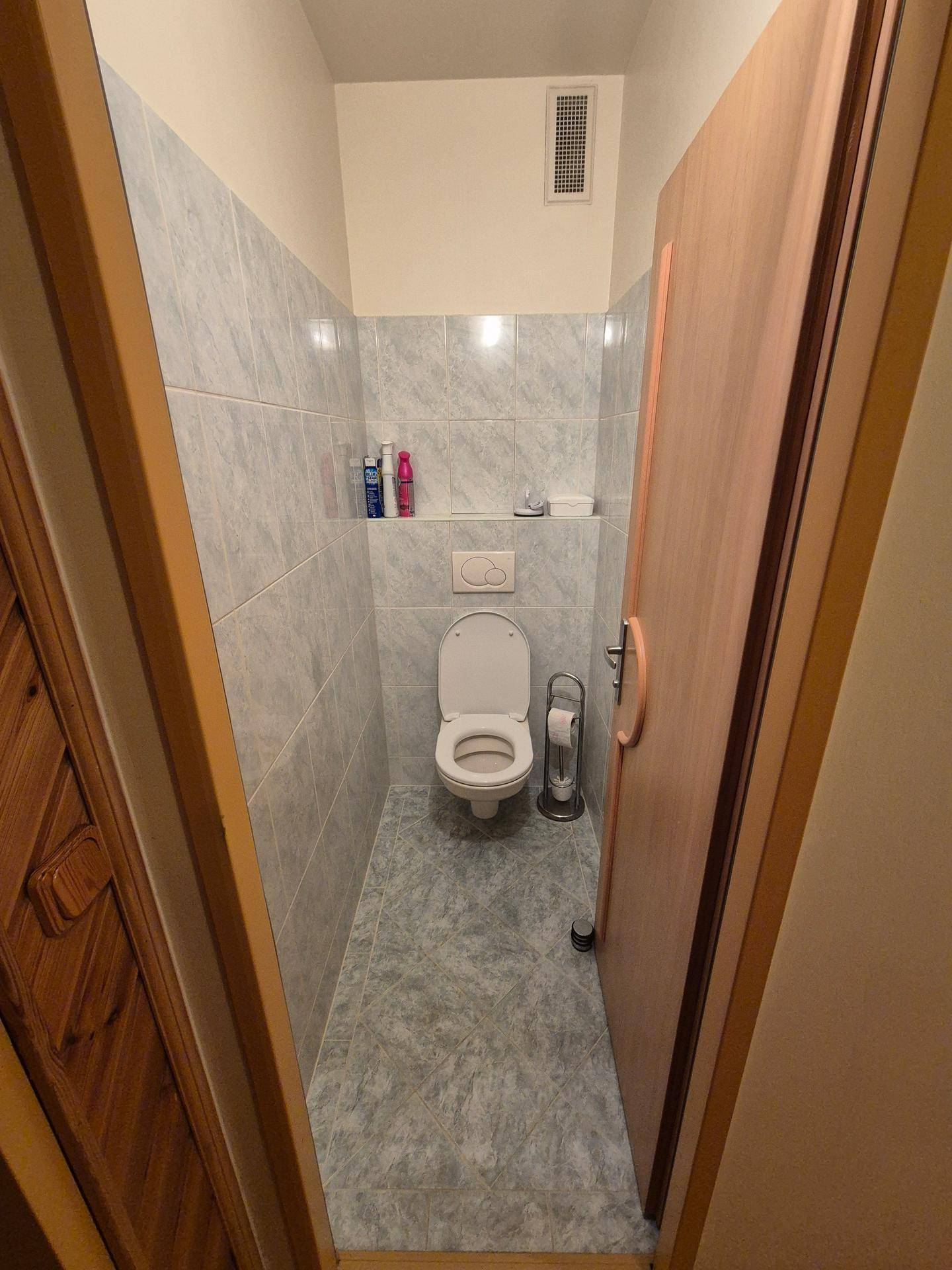 Separate Toilette mit Wandfliesen und einem Lüftungsgitter an der Decke.