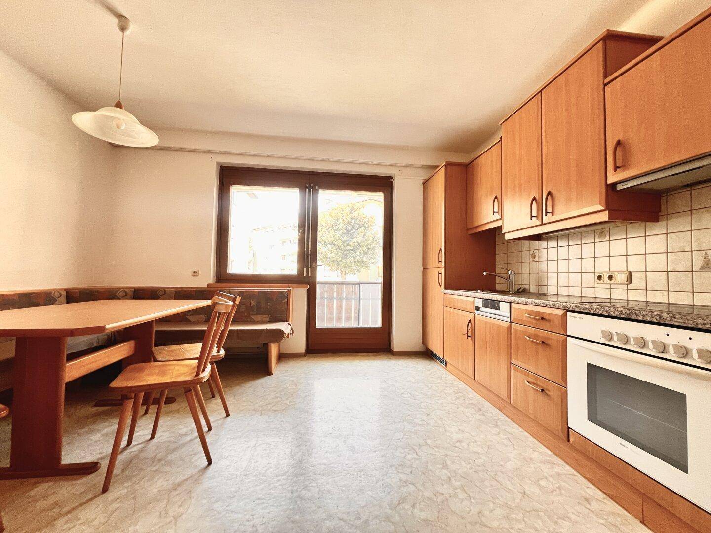 Gemütliche Wohnküche mit traditionellen Holzschränken, Essbereich und Zugang zu einem Balkon.