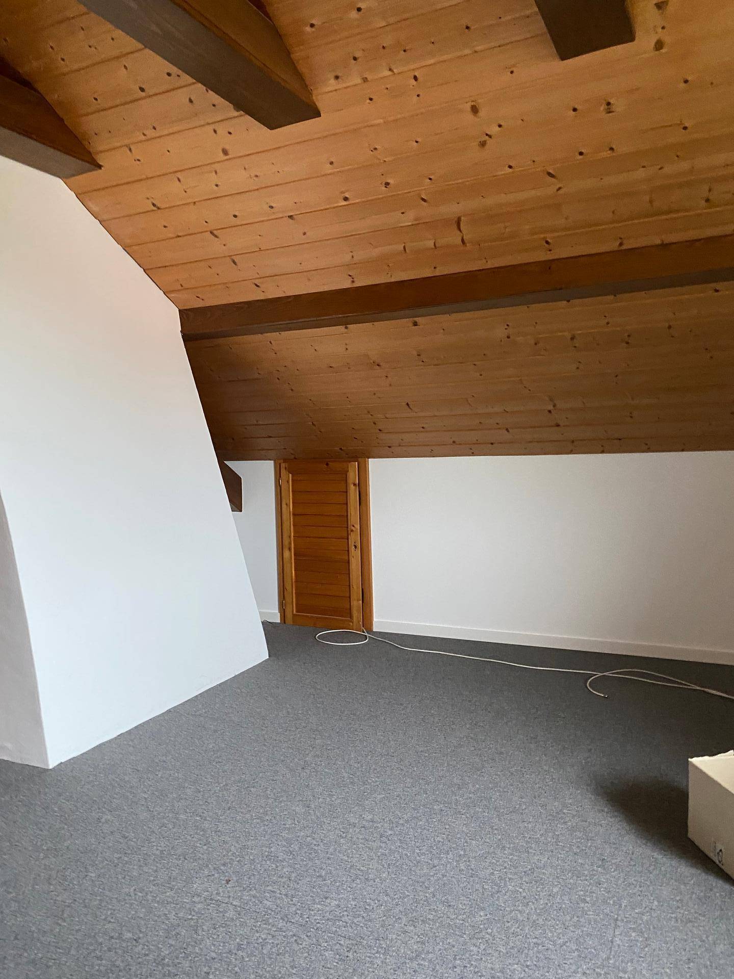 Dachgeschosszimmer mit Teppichboden, Holzbalkendecke und Dachschrägen.