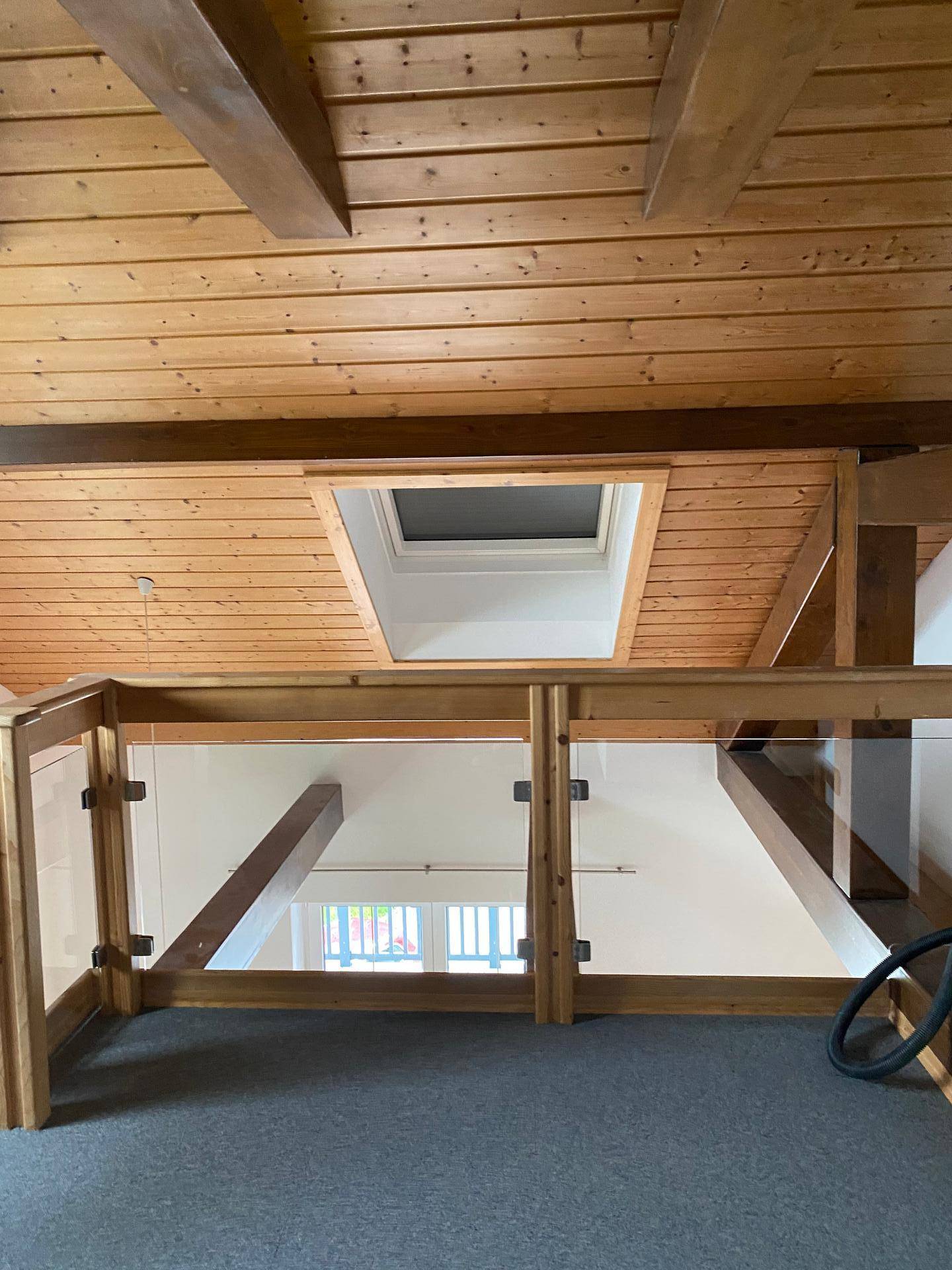 Offener Galeriebereich mit Glasgeländer, Holzbalkendecke und Dachfenster.