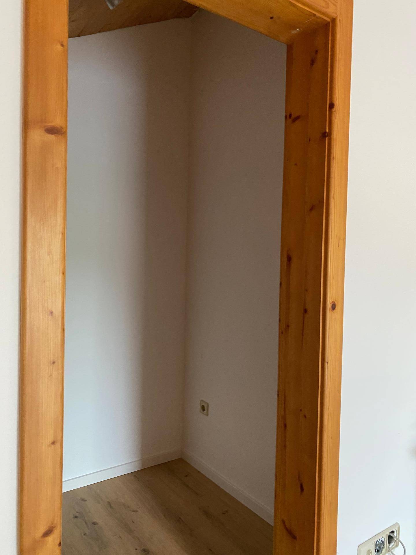 Kleiner Abstellraum oder Nische mit Holztürrahmen und Steckdose.