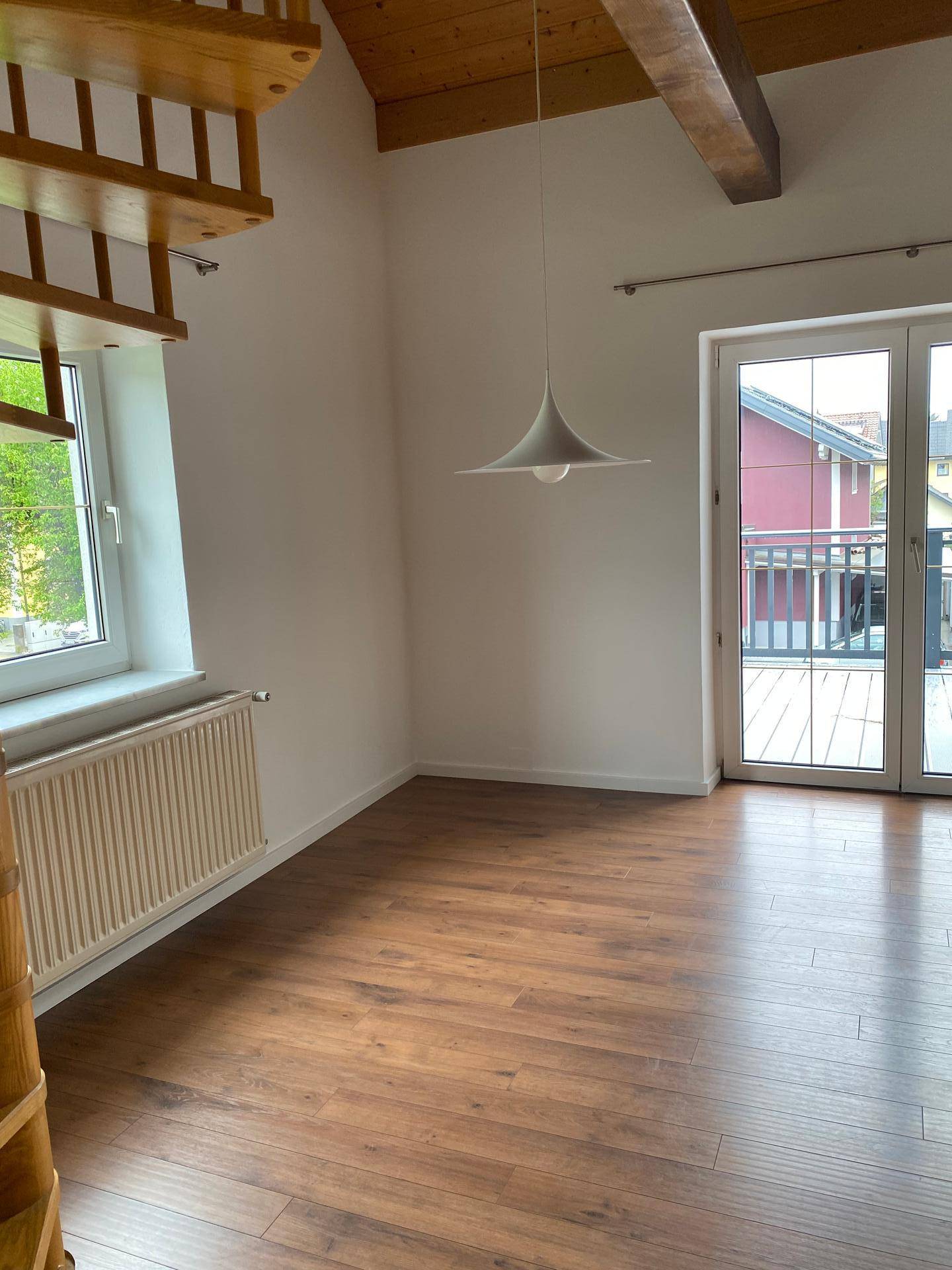 Heller Wohnraum mit Laminatboden, Dachschräge und Zugang zu einem Außenbereich.