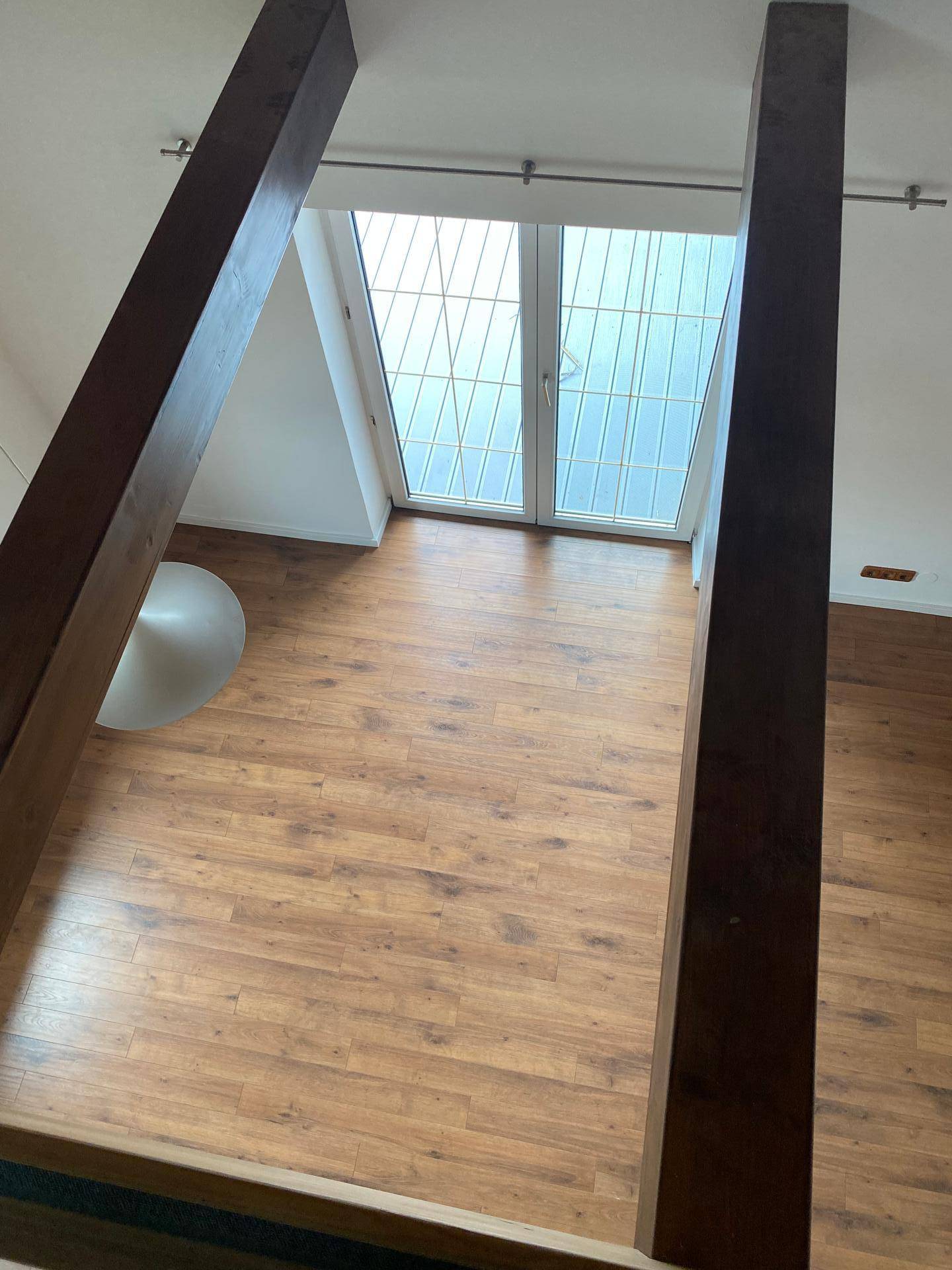Blick von oben in einen hellen Wohnbereich mit Laminatboden und großen Fenstern.
