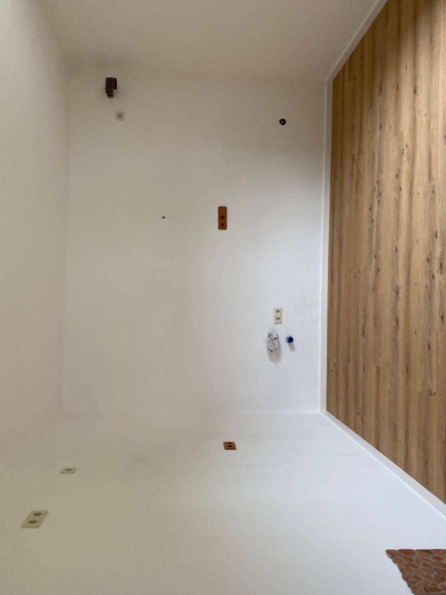 Leerer Küchenraum mit Anschlüssen für Geräte und einer Holzwandverkleidung.