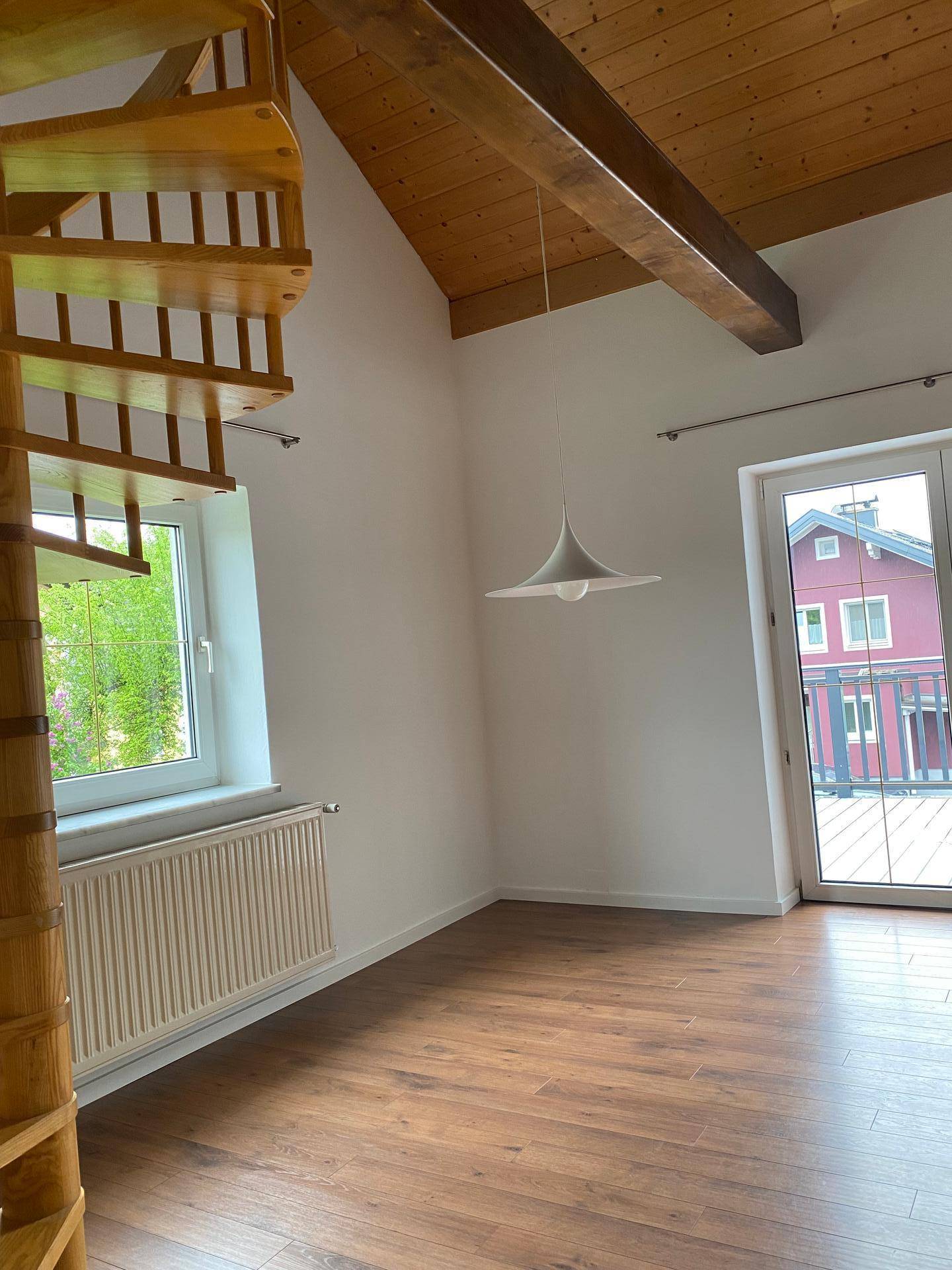 Geräumiger Wohnbereich mit Holzbalkendecke, Laminatboden und Zugang zu einem Balkon.
