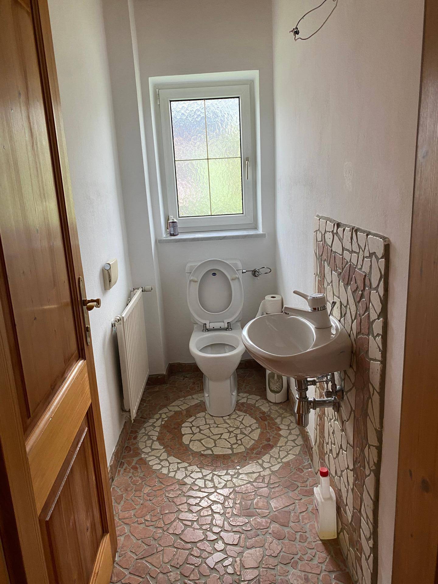 Gäste-WC mit Mosaikfliesen, Fenster und kleinem Waschbecken.