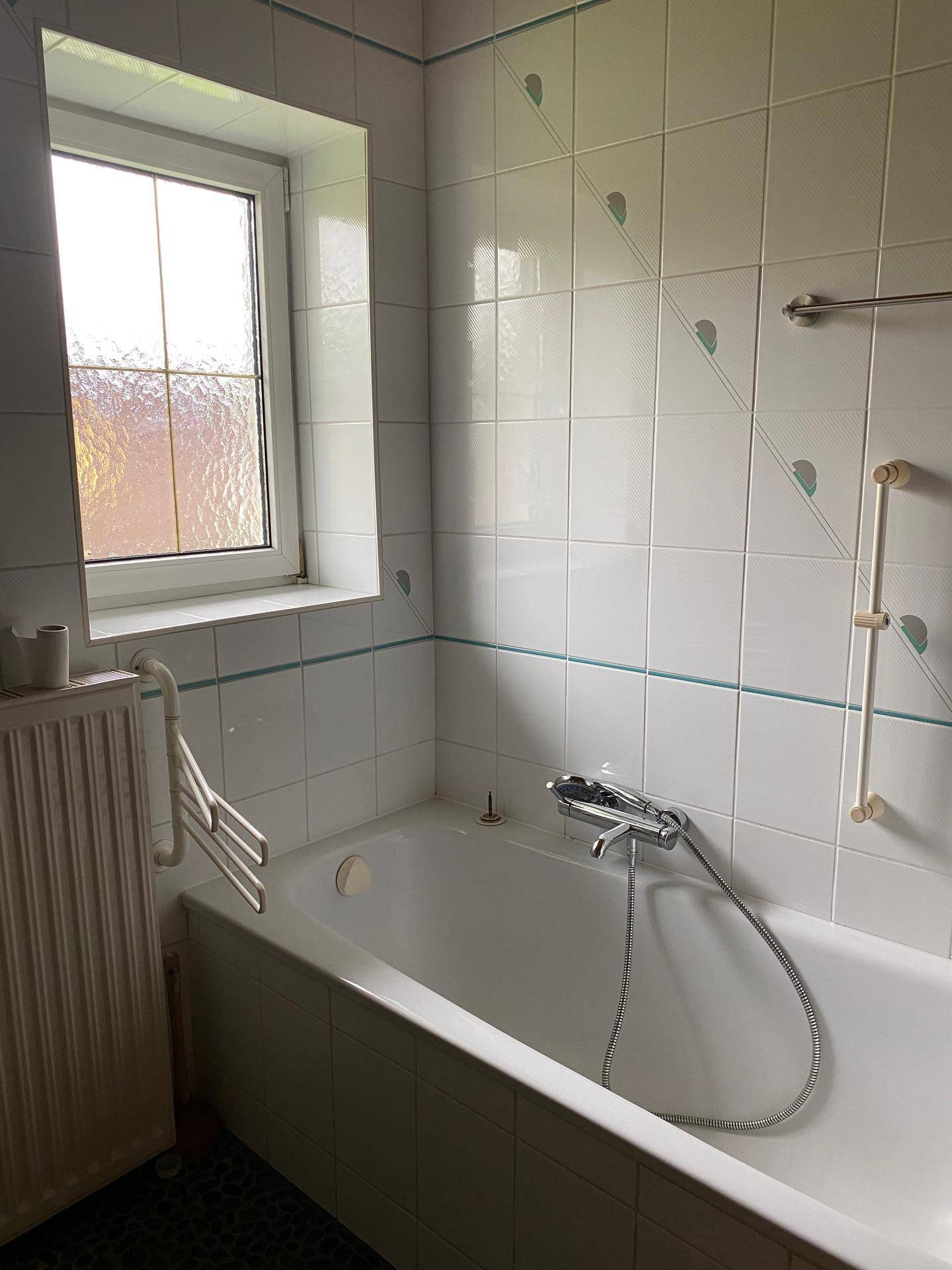 Badezimmer mit Badewanne, weißen Fliesen und Fenster.