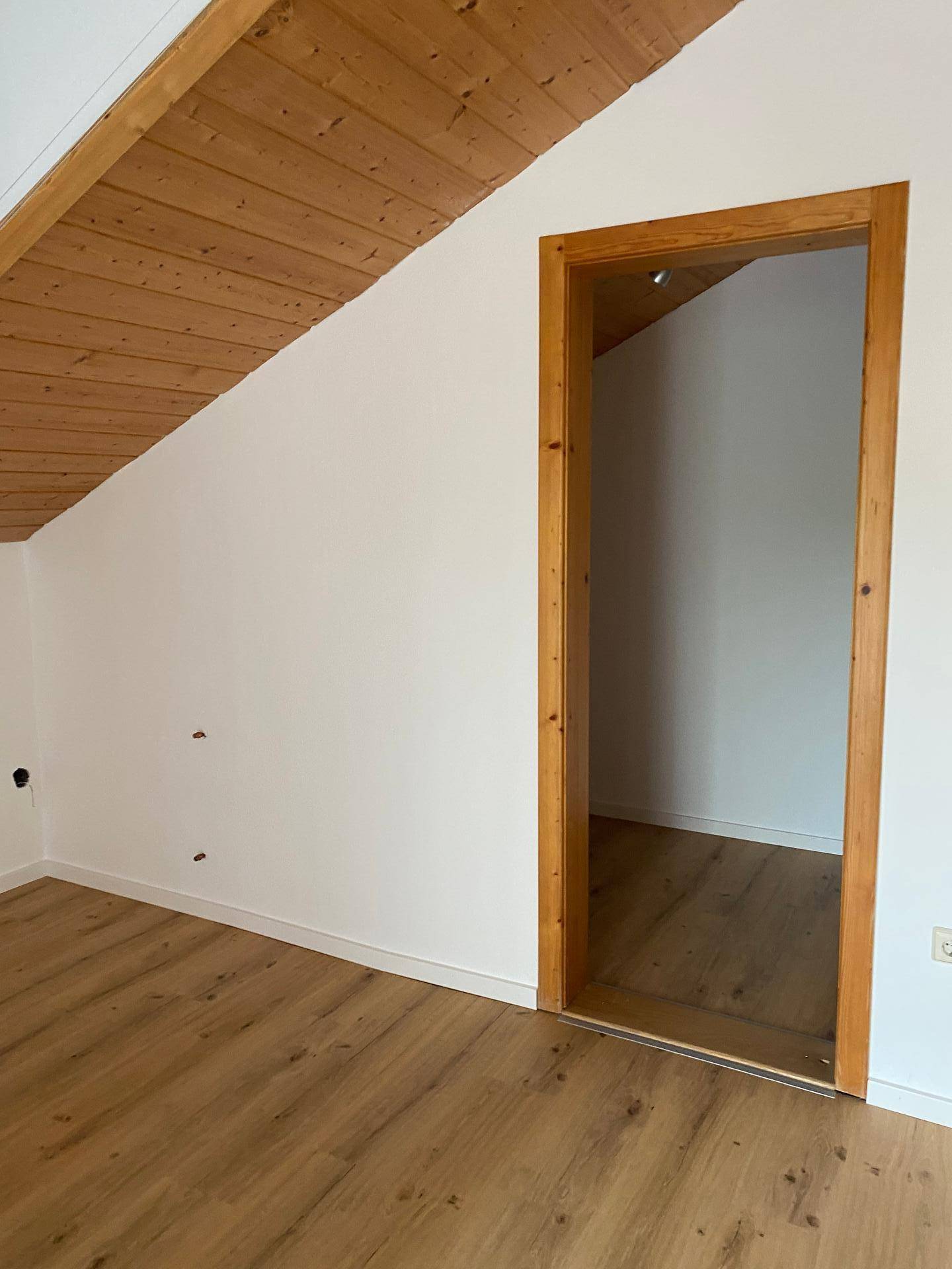Leerer Raum mit Holztürrahmen, Dachschräge und Laminatboden.