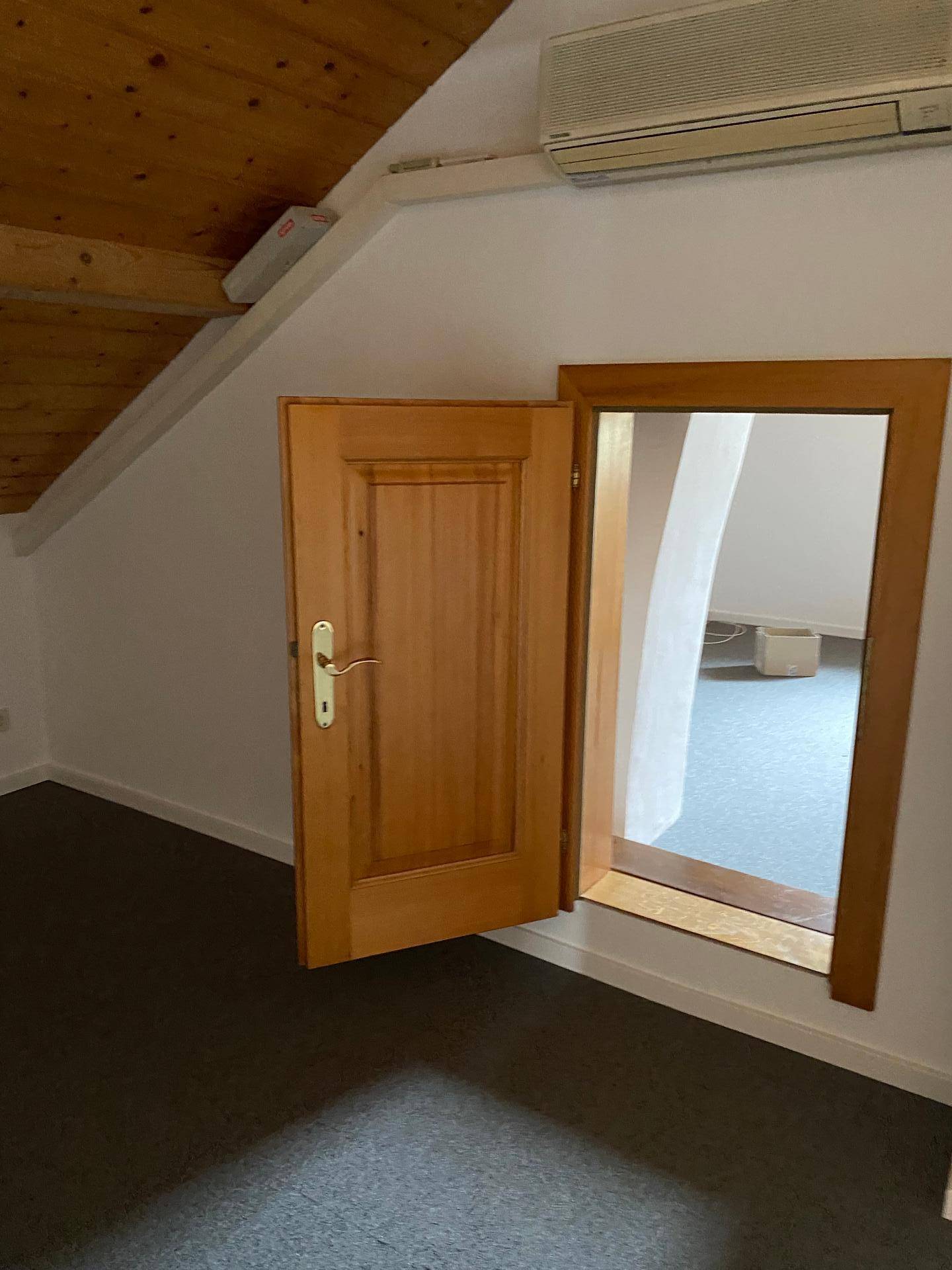 Dachgeschosszimmer mit Teppichboden, Holztür und Klimaanlage.