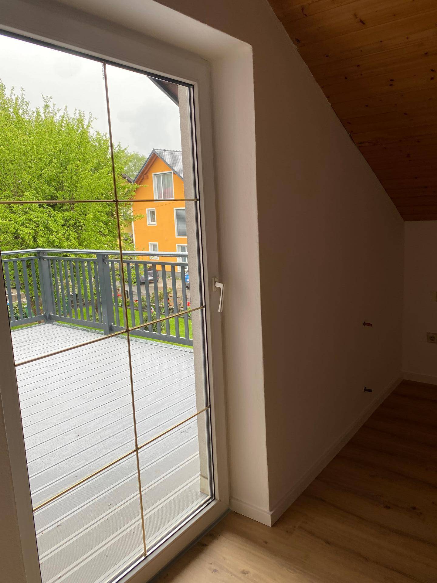 Geräumiger Balkon mit grauem Bodenbelag und Blick auf die umliegenden Häuser und Bäume.