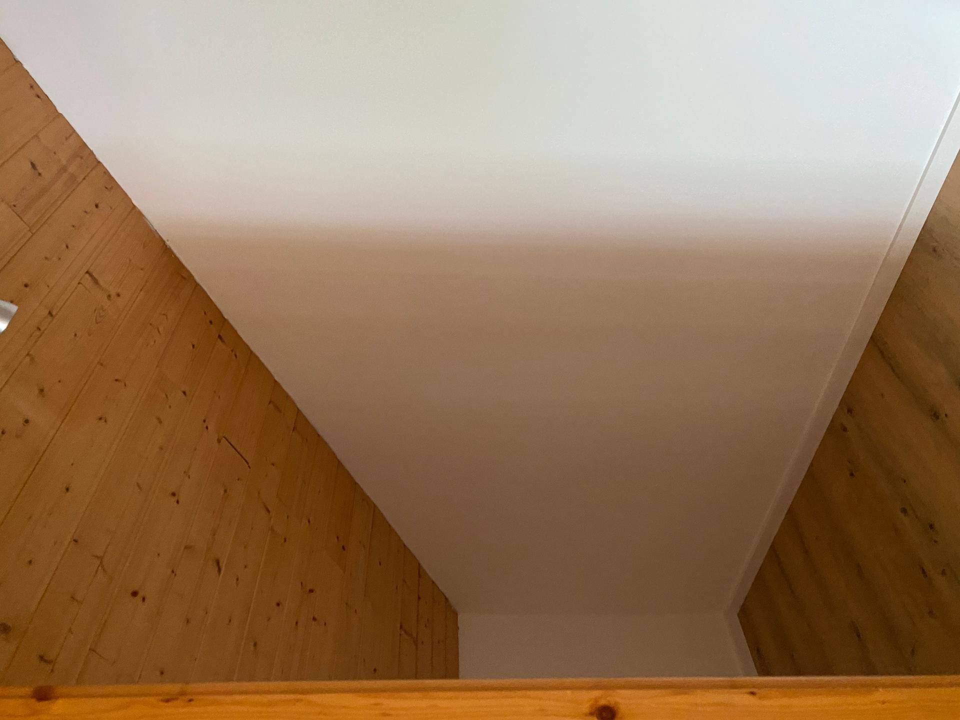 Dachschräge mit Holzverkleidung und weiß gestrichenen Wänden.