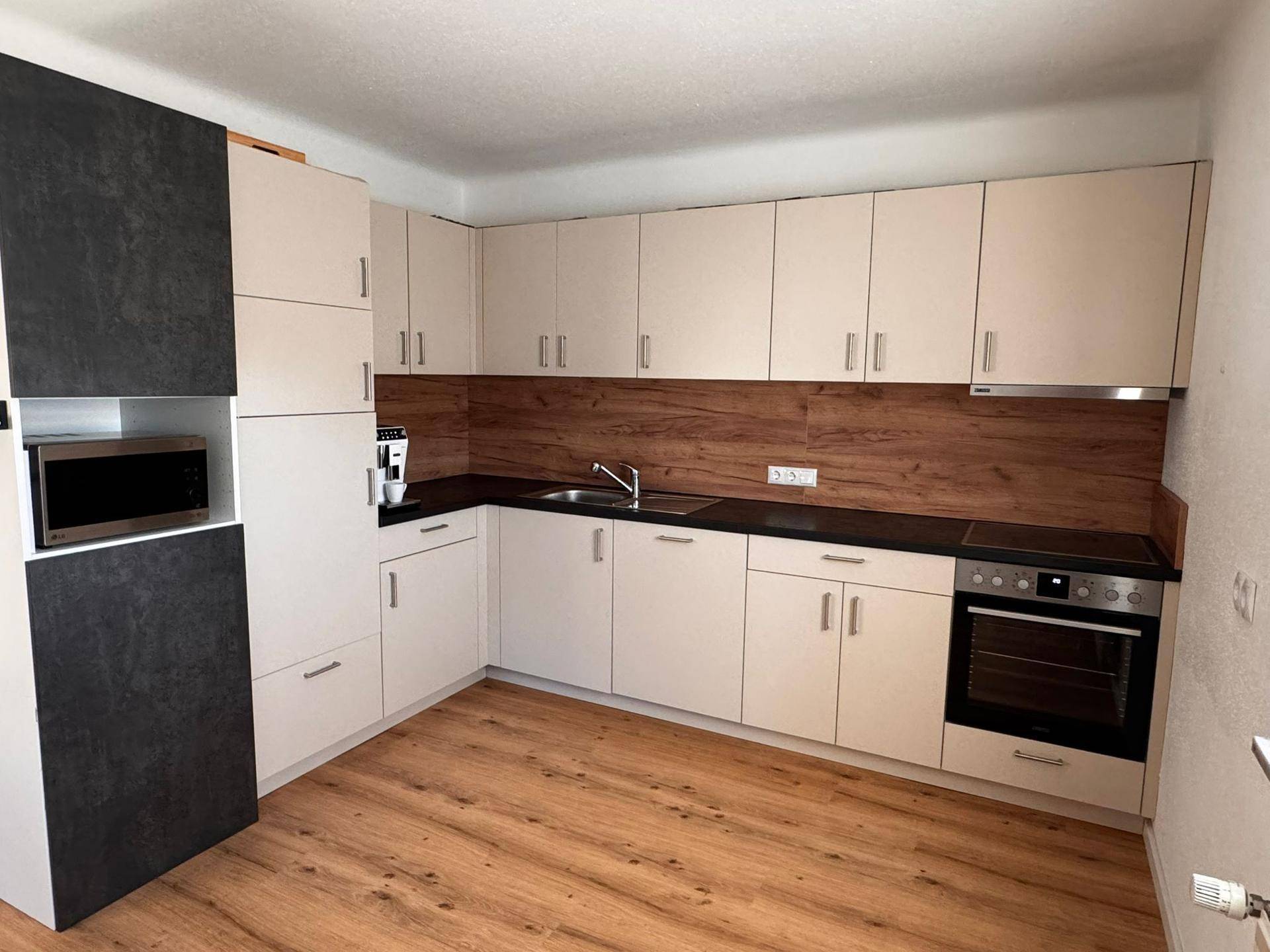 Moderne Einbauküche mit hellen Schränken, dunkler Arbeitsplatte und Holzakzenten.