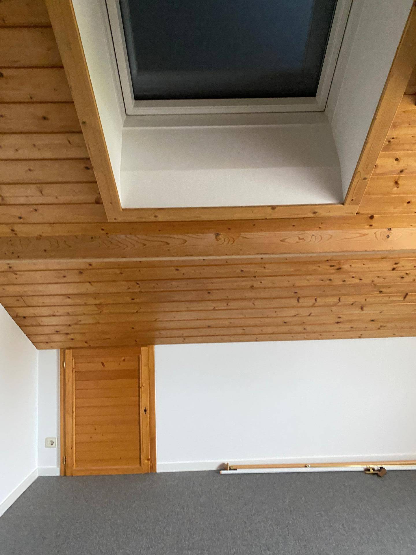 Helles Dachzimmer mit Holzdecke, Dachfenster und Teppichboden, bereit zur individuellen Gestaltung.