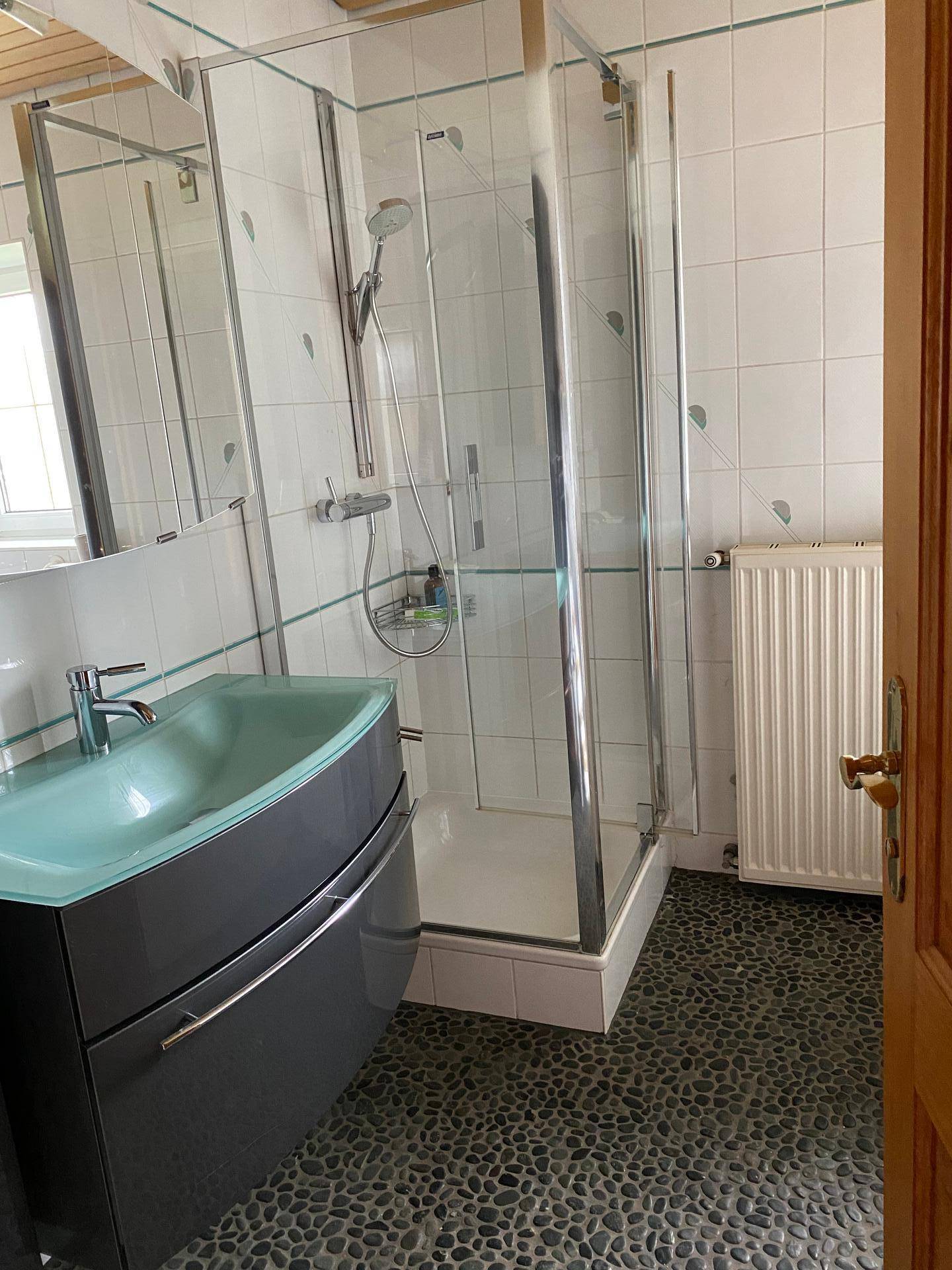 Badezimmer mit Duschkabine, modernem Waschtisch und Kieselsteinboden.