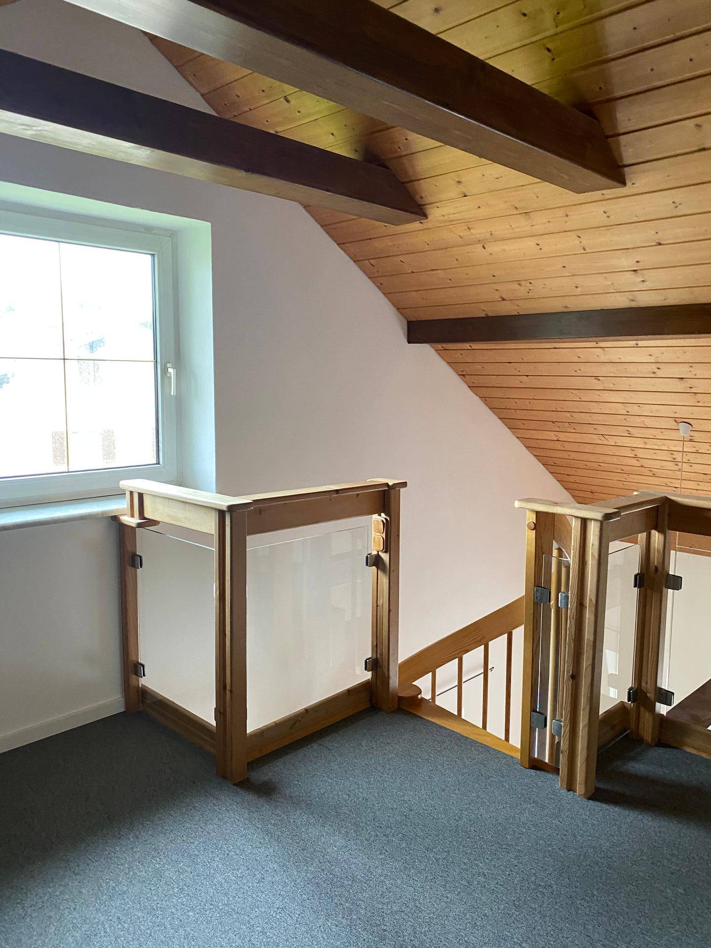 Dachgeschoss-Flur mit Holzverkleidung, sichtbaren Balken und Fenster, das viel natürliches Licht hereinlässt.
