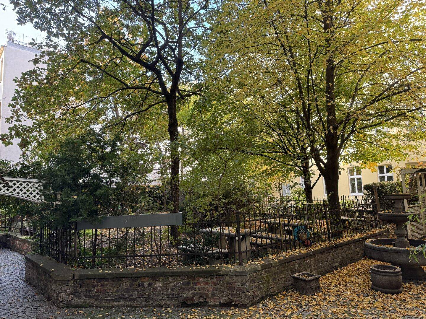 Ruhiger Innenhof mit altem Baumbestand, Ziegelmauer und einem dekorativen Brunnen.