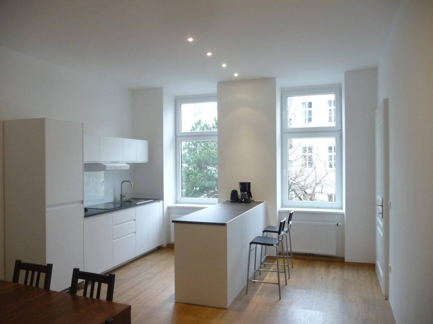 Moderne offene Küche mit weißer Einbauküche, Kücheninsel und Holzboden.