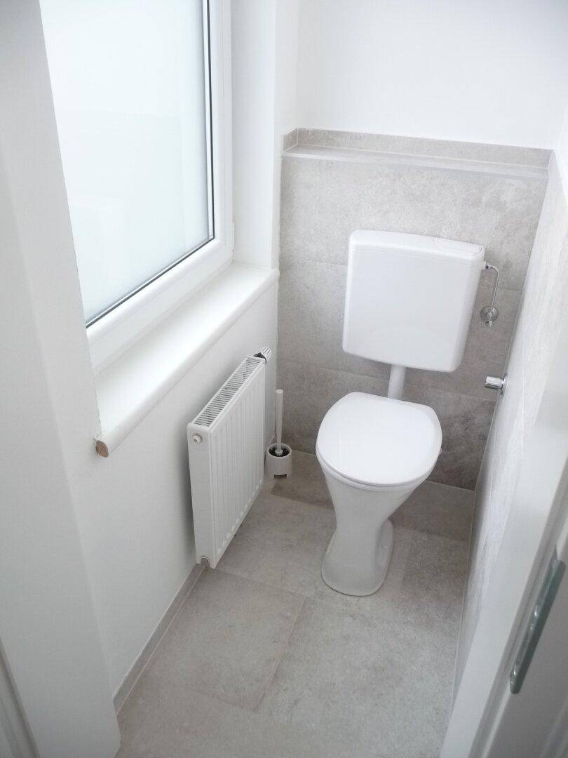 Separates WC mit Fenster, Toilette und Heizkörper, hell gefliest.