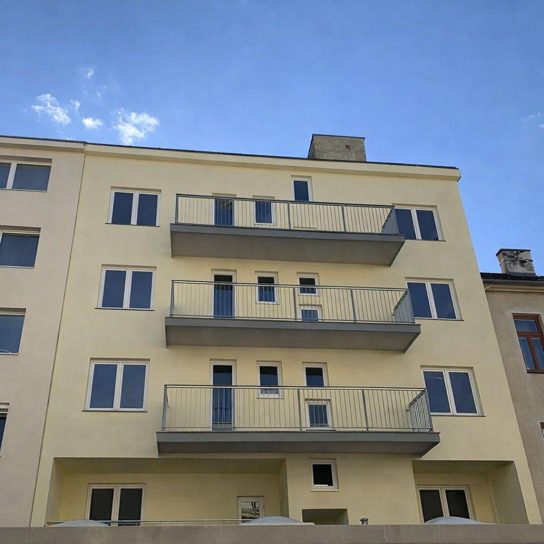 Moderne Gebäudefassade mit mehreren Balkonen und klaren Linien unter blauem Himmel.