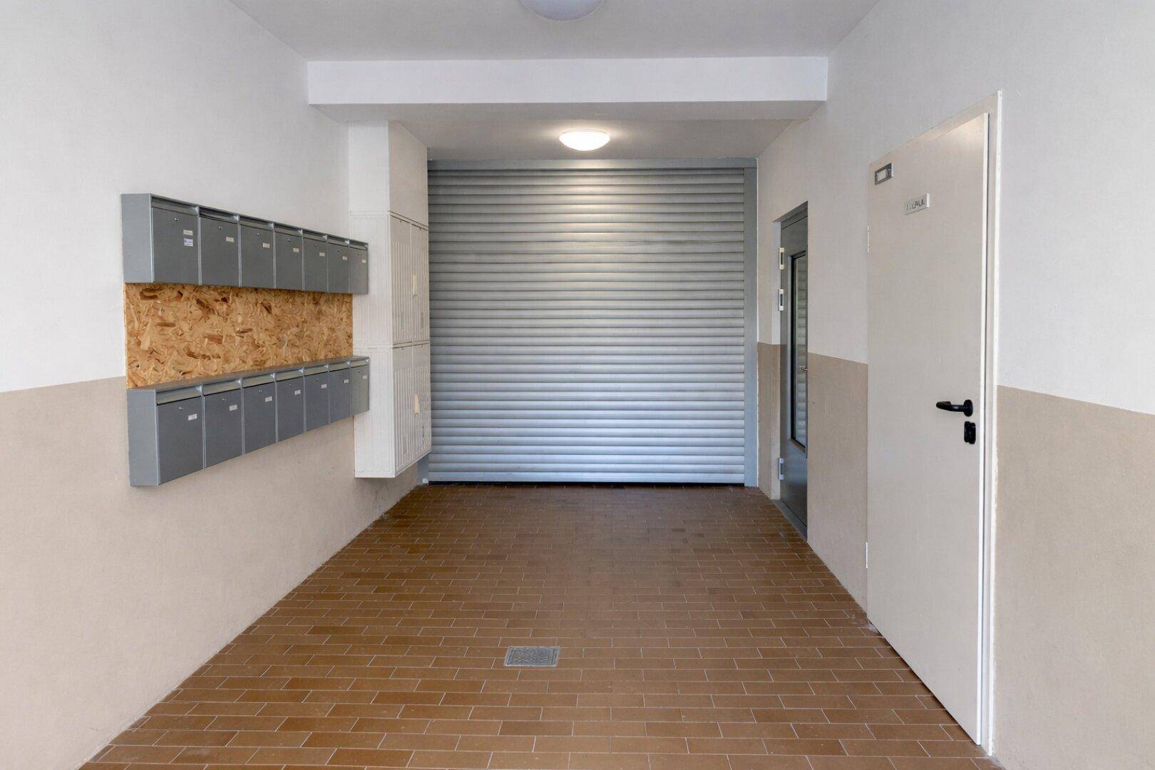 Eingangsbereich eines Wohnhauses mit Briefkästen und einem Rolltor im Hintergrund.