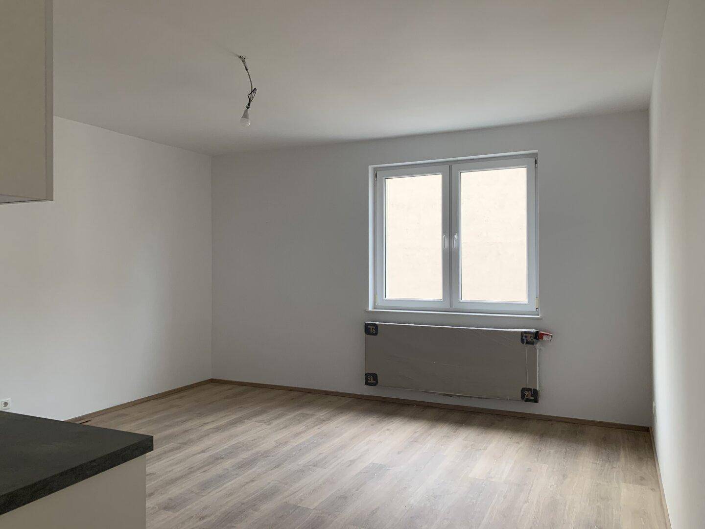Heller Raum mit großem Fenster, Heizkörper und neuem Laminatboden.