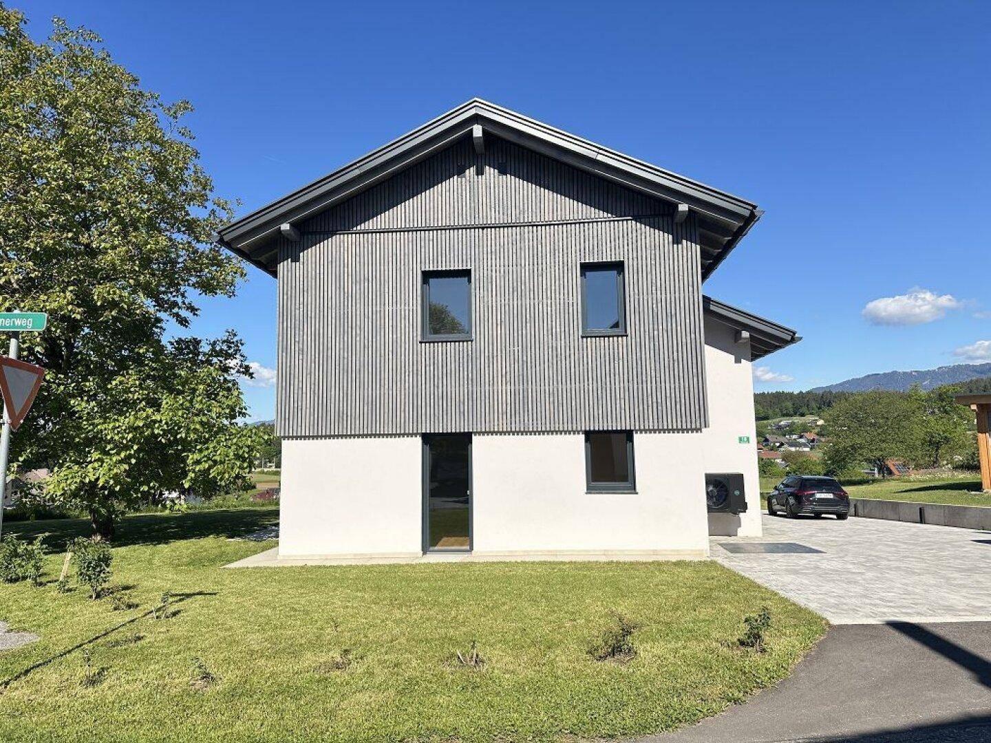 Moderne Hausfassade mit Holzverkleidung und weißem Putz, umgeben von gepflegtem Rasen.