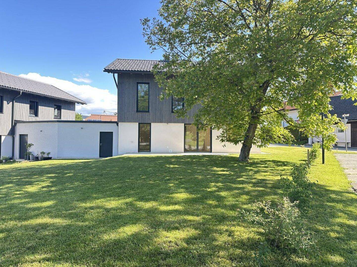 Rückansicht des modernen Hauses mit großer Rasenfläche und Baumbestand im Hintergrund.
