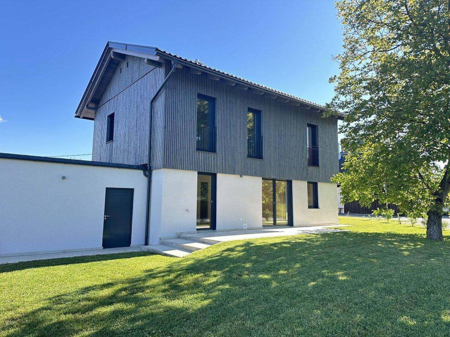 Moderne Architektur mit Holzfassade und weißem Putz, umgeben von einer weitläufigen Rasenfläche.