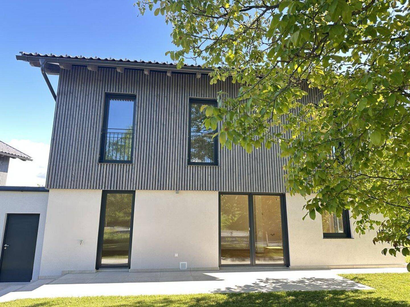 Hinterer Bereich des Hauses mit großer Terrasse und Zugang zum Garten, umgeben von Grün.
