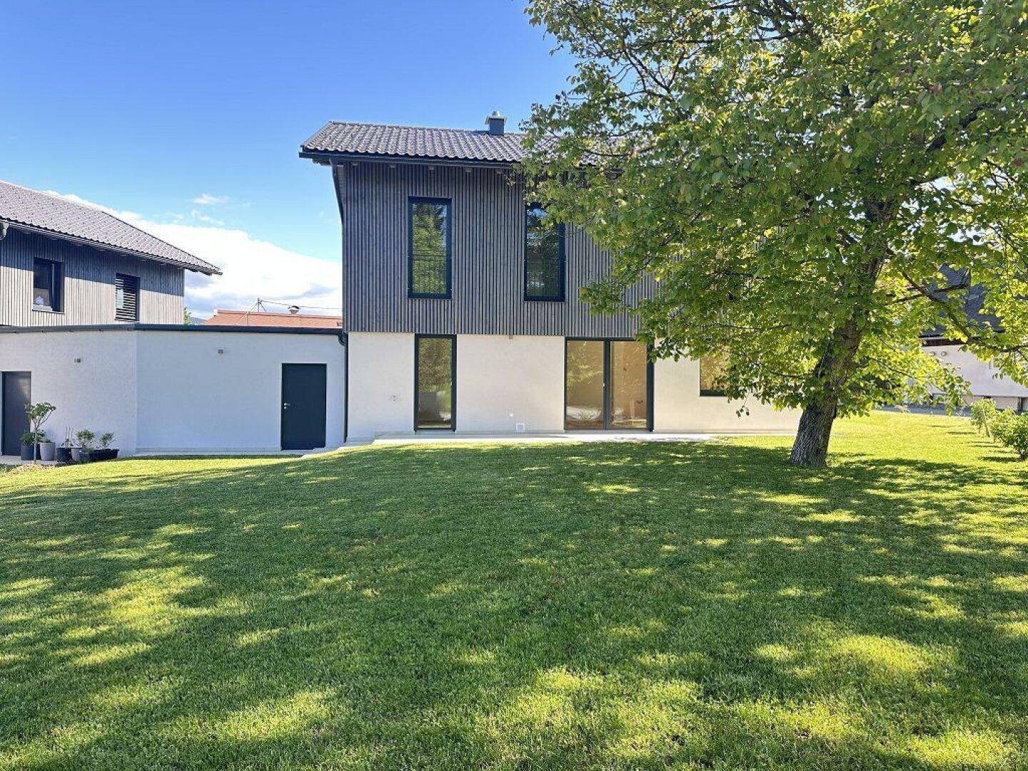 Rückseite des modernen Hauses mit großer Rasenfläche und gepflastertem Bereich.