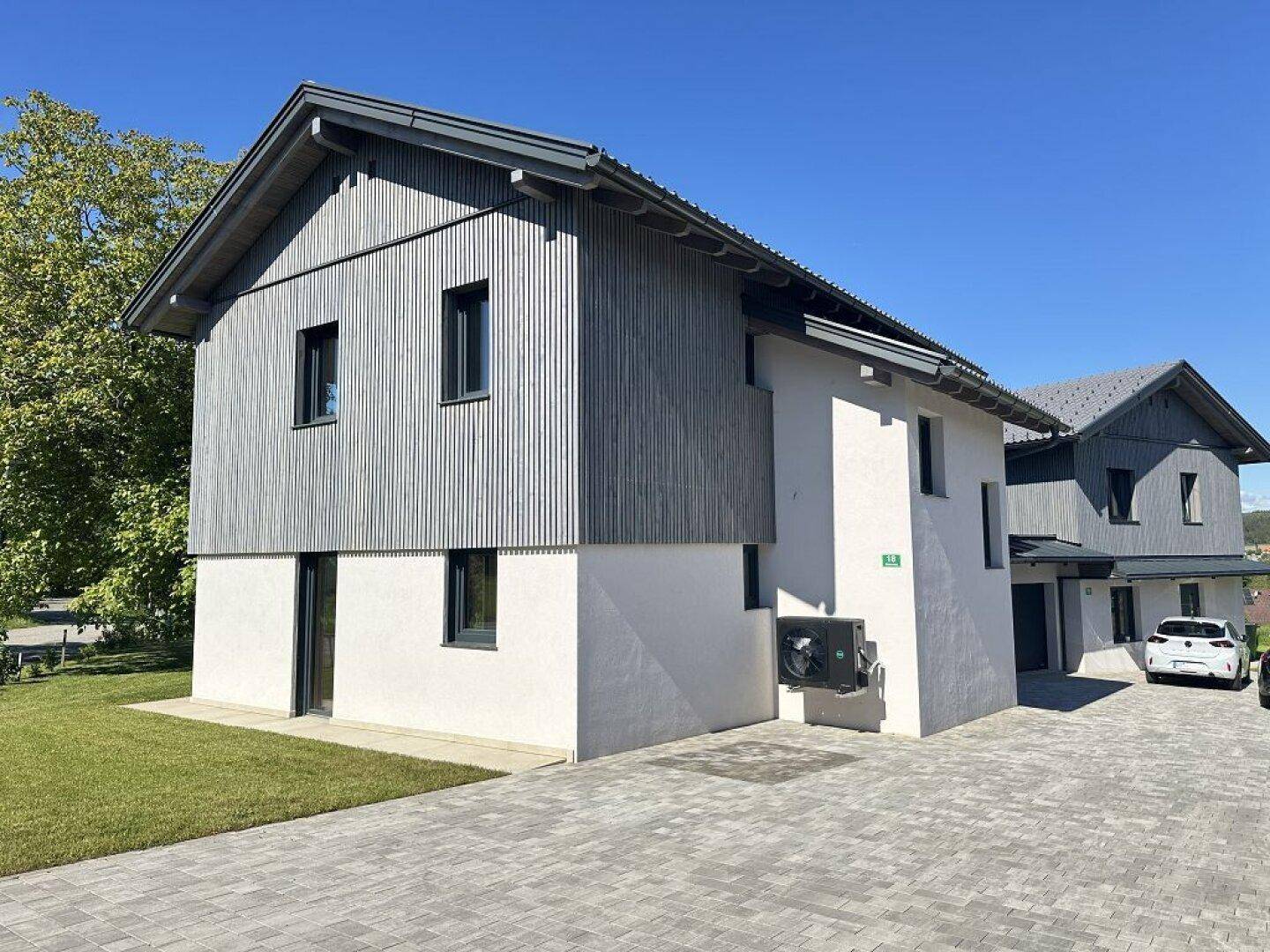 Modernes Doppelhaus mit Holzverkleidung und gepflasterter Einfahrt unter blauem Himmel.