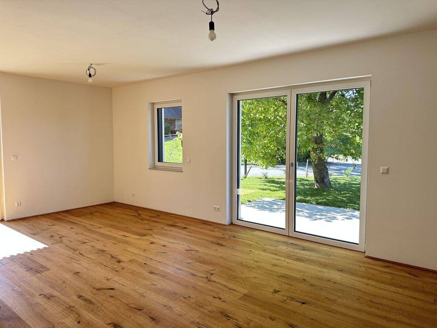 Heller Wohnraum mit Eichenparkettboden und großen Fenstern mit Blick ins Grüne.