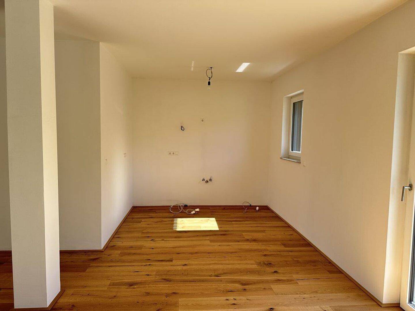 Leerer Raum mit Holzboden und Fenster, vorbereitet für eine moderne Küche.
