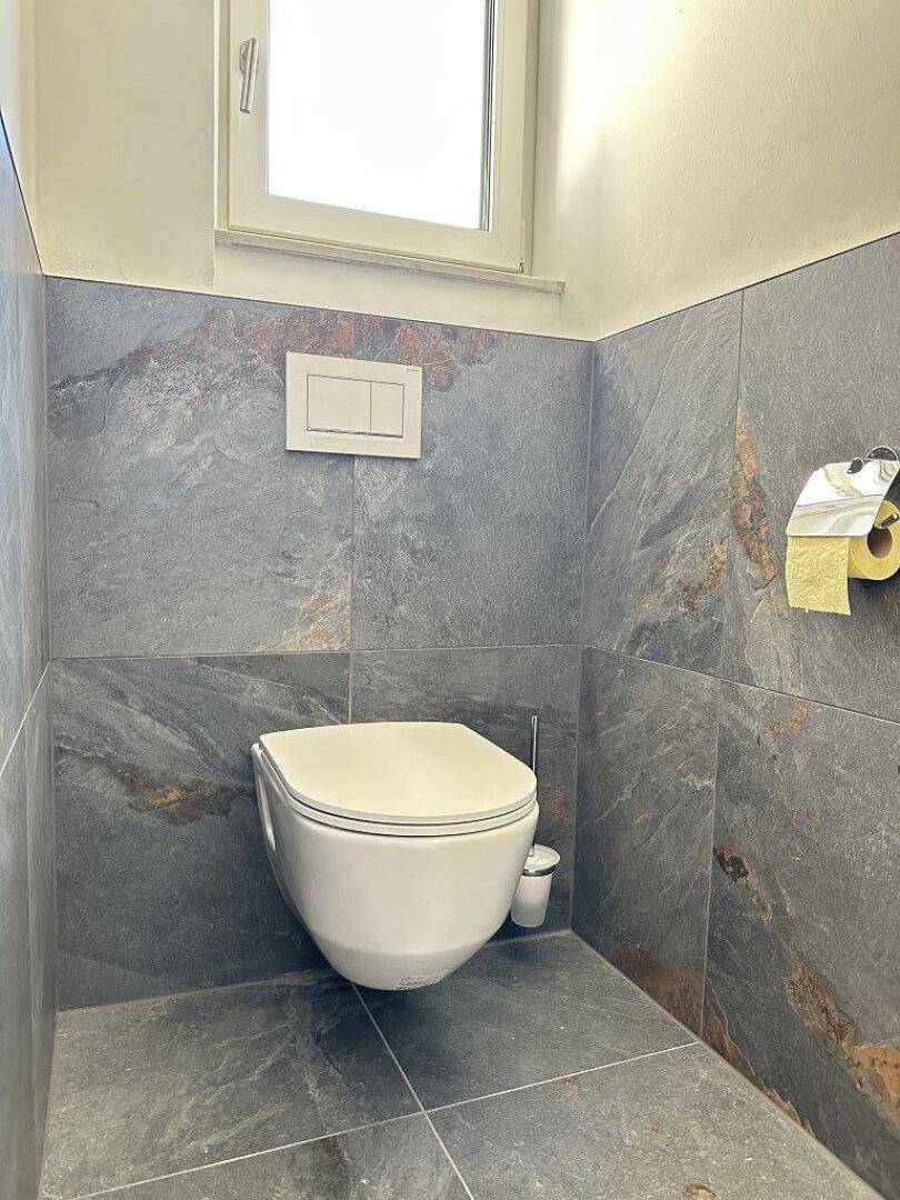 Modernes Gäste-WC mit dunklen Fliesen und wandhängendem WC, ausgestattet mit Fenster.