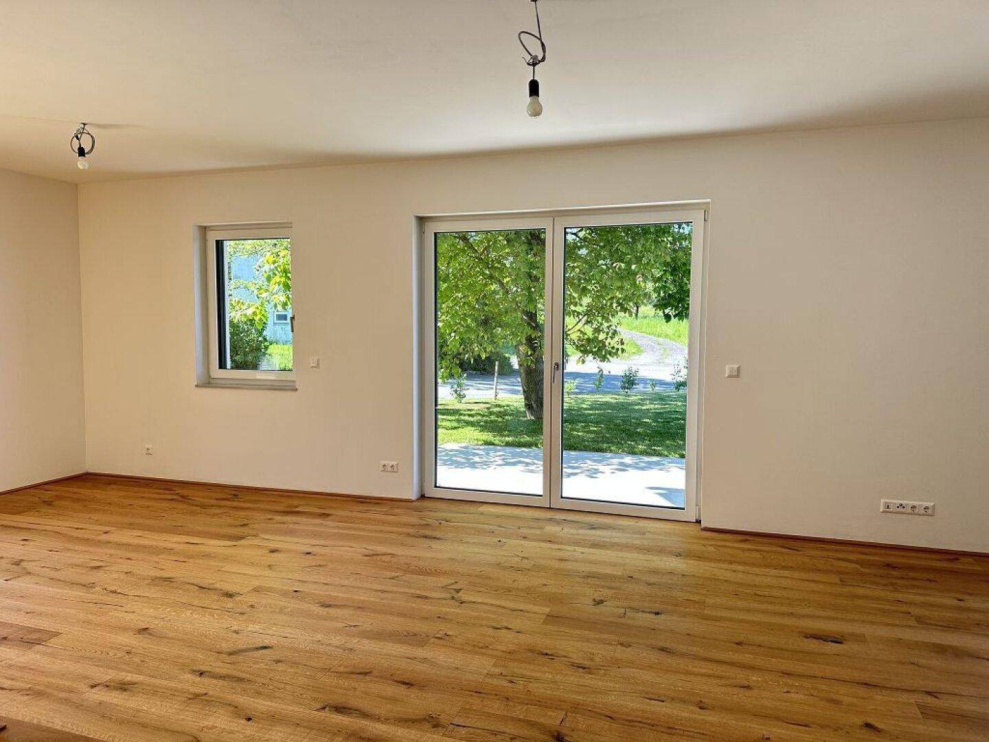 Heller Wohnraum mit Eichenparkettboden und großen Fenstern mit Blick ins Grüne.