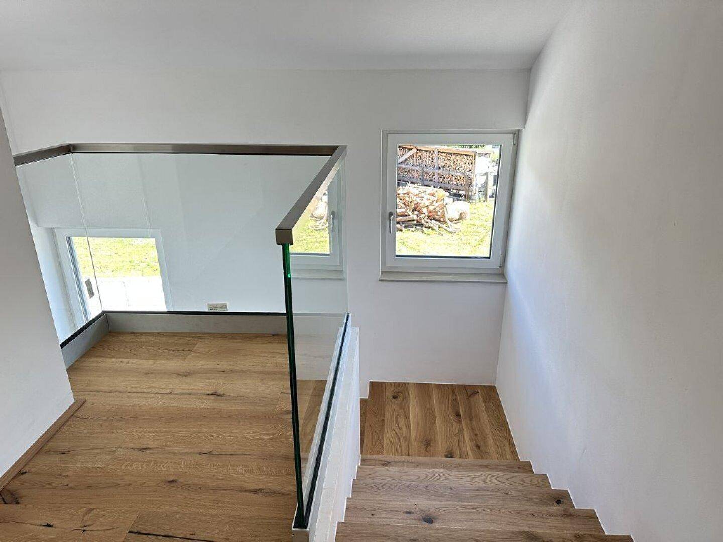 Treppenaufgang mit Holzstufen und Glasgeländer, bietet Blick auf den Außenbereich.